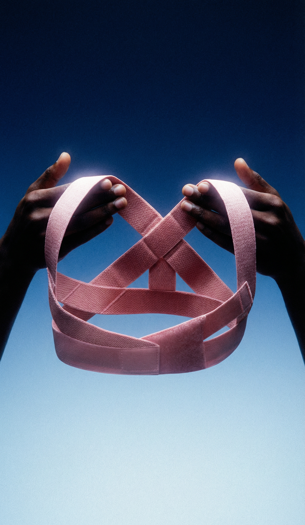 Pink ribbon held by two hands against a blue background