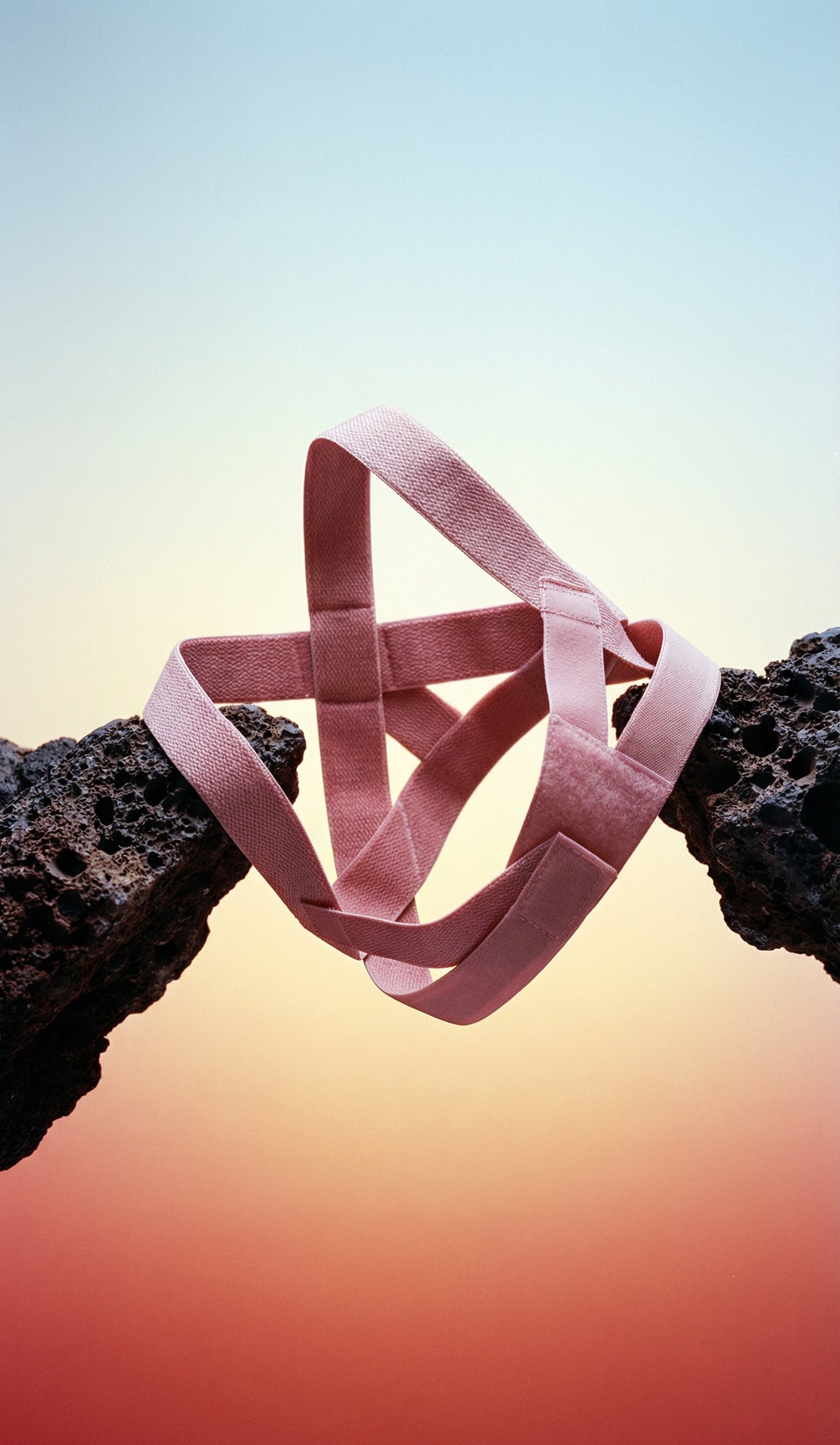 Pink back brace stretched between two rocks with a gradient background
