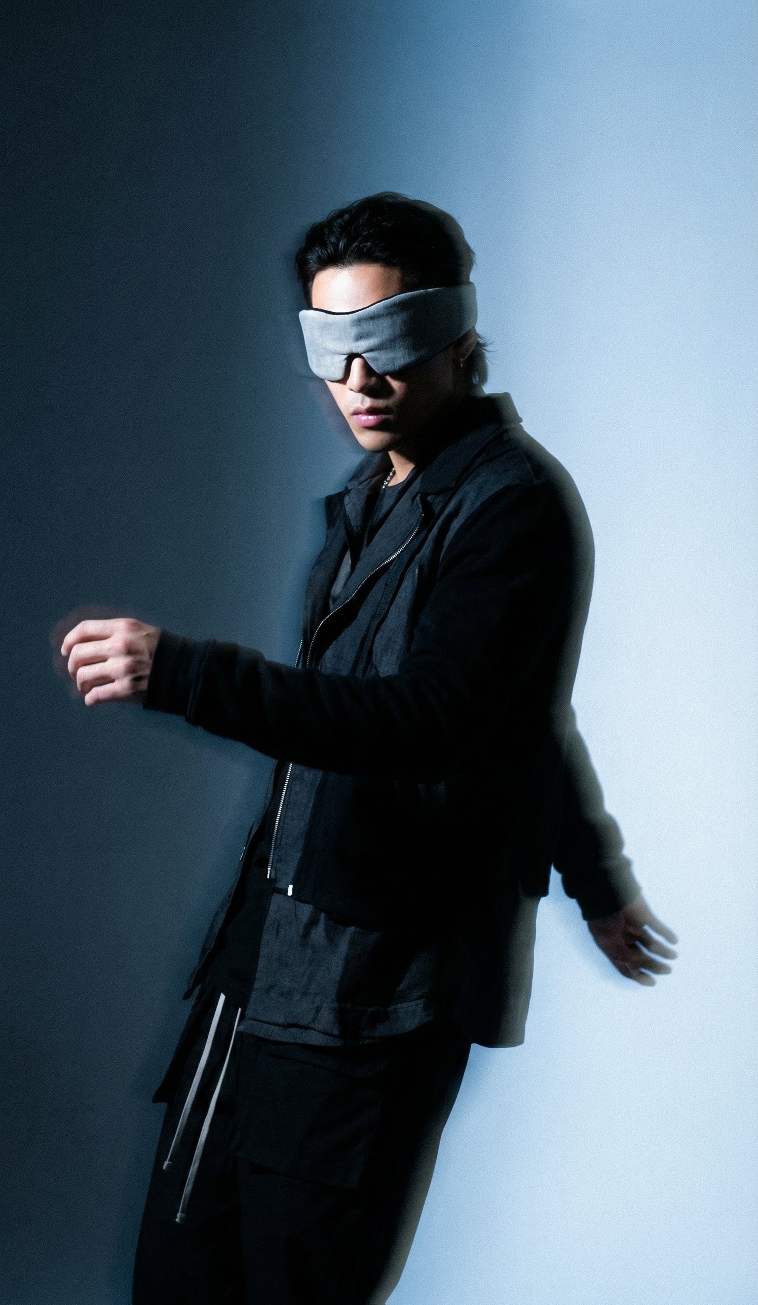 Person wearing a black suit and blindfold against a gradient background