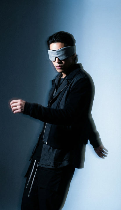 Person wearing a black suit and blindfold against a gradient background